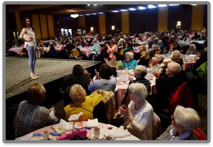 A model poses at the end of the runway during the Lackawanna Blind Association's Helen Keller Day Fashion Show, with a large audience gathered, enjoying the show.