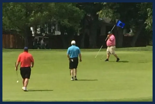 Three golfers participating in the Swing for Sight Golf Tournament. On is carrying a blue flag as the others approach the hole.